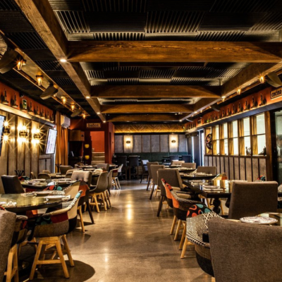 An interior view of Cometa restaurant, featuring a modern and warm atmosphere, set tables, and colorful chairs beneath a lit wooden ceiling.