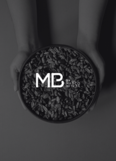 A bowl of grains held in the hands, featuring the logo of MB by Marco Beteta, a culinary guide that recognizes KOLI’s culinary offerings.